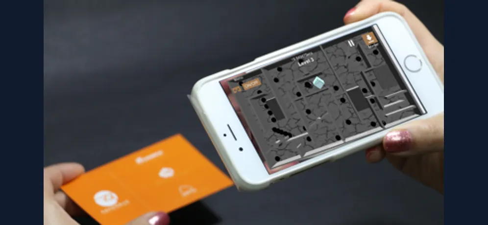 An iPhone displaying the ARVR Maze game, with an orange card held beside it